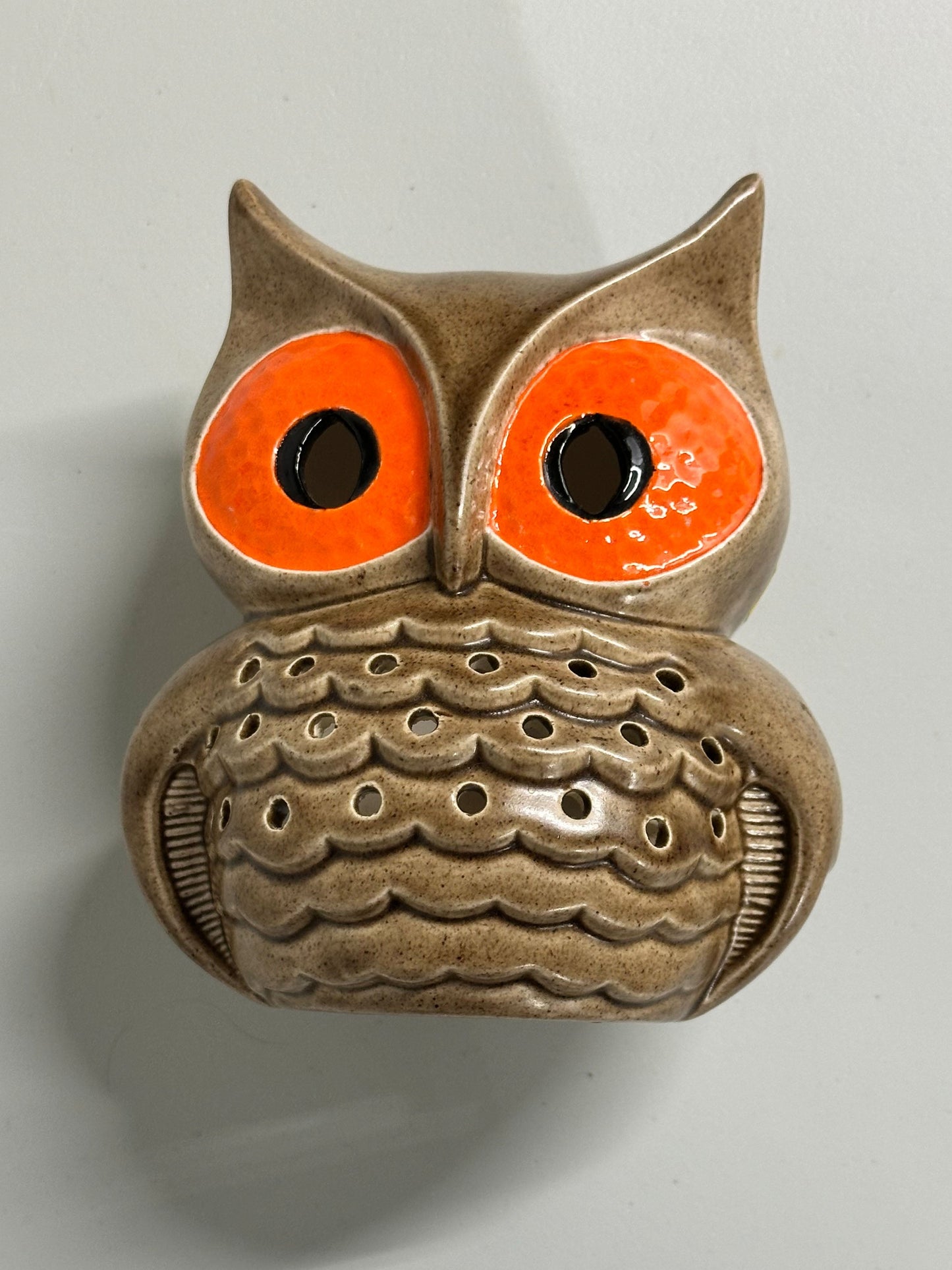 Ceramic owl-shaped decorative item with orange eyes on a gray background