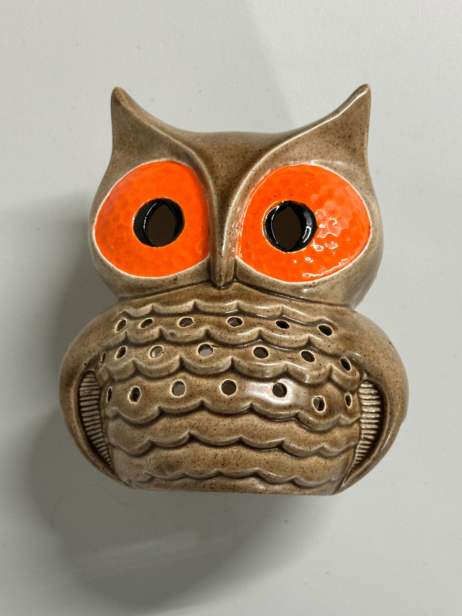 Ceramic owl-shaped decorative item with orange eyes on a gray background